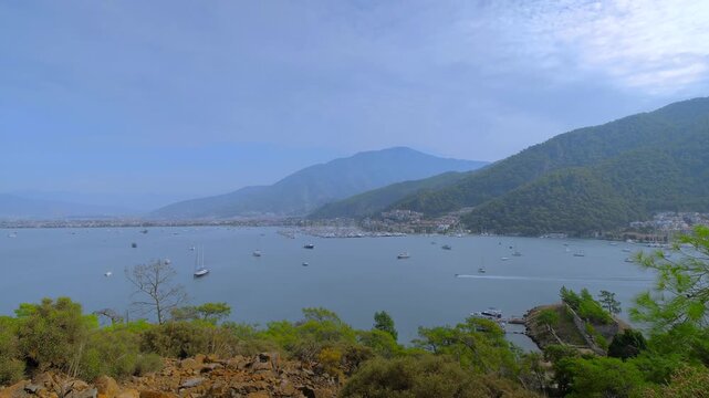 Time lapse: anchored yachts and gulets in Fethiye bay, some boats are gliding fast across the water against lush mountain backdrop. Marine tourism, timelapse and travel concept