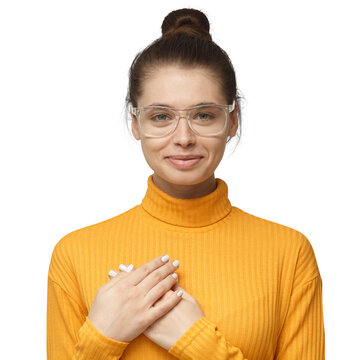 Lovely woman in yellow polo neck sweater having charming smile and friendly expression holding hands on her heart, showing her love and sympathy.