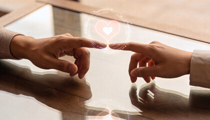 This high-quality conceptual image features two individuals connecting through a delicate touch of their fingertips on a polished, reflective glass table. A luminous, digital holographic heart icon is