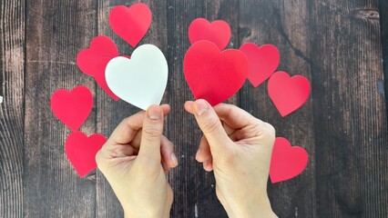 Hands holding red and white paper heart cutouts against a rustic wooden background
