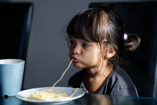 Cute childhood emotion during eating. Kid eating spaghetti meal at home. Messy spaghetti mouth and lips moment. Portrait of toddler eating pasta indoors. Cute girl slurping noodles during dinner.