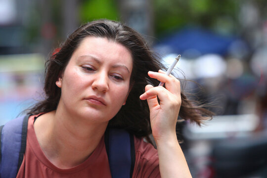 Close-up portrait of a thoughtful adult woman smoking a cigarette outdoors on a city street. 