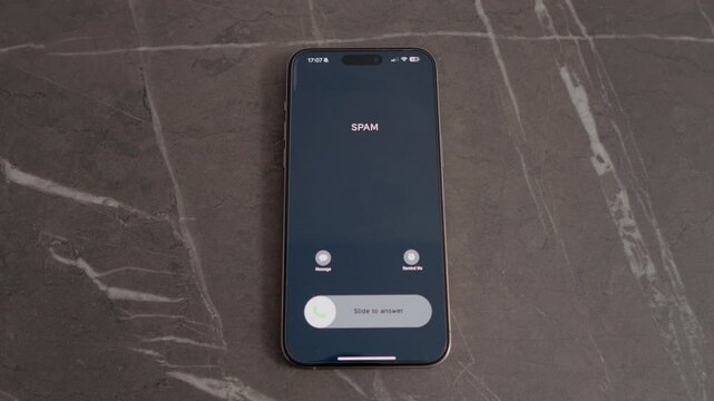 A smartphone displays an incoming call labeled as spam while resting on a table. The user must decide whether to answer or ignore this call.