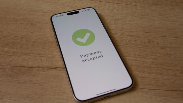 A smartphone displays an accepted payment on its screen. The phone is placed on a wooden table, clearly showing the successful transaction process.