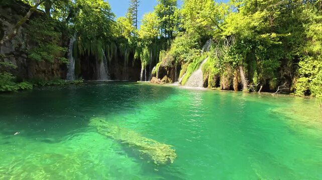 A breathtaking view of multiple waterfalls cascading over limestone tufa barriers into turquoise pools in Plitvice Lakes National Park, Croatia. Lush green vegetation and moss cover the rocks around