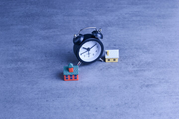 Two model houses with blurred clock in background suggest themes of home ownership, real estate timing, and housing-related decisions.