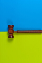 Wooden judge gavel on blue and yellow-green background, symbolizing law, justice, and authority in a visually striking composition.
