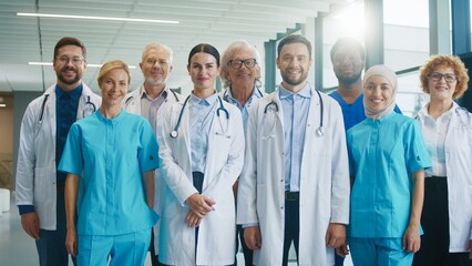 Medical team standing together in bright hospital corridor. Smiling confidently. Showing unity and professionalism while posing for group portrait during active clinical routine. Healthcare concept.