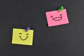 Yellow and pink sticky notes with smiley faces on black background, expressing emotion and contrast through minimal design and color.