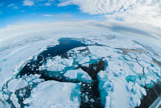 Arctic Ocean sea ice and ice floes breaking up and melting, depicting environment, global warming, and climate change impacts with dark water visible under a wide blue sky