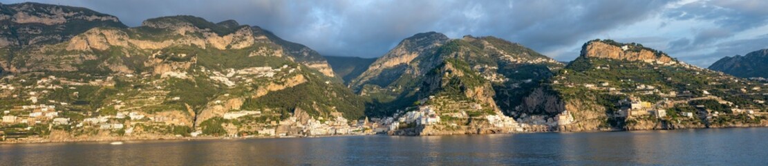 Fototapeta premium Pastel villages tumble down Amalfi's sheer cliffs like sun-kissed confetti, their terraced lemon groves and ochre tiles aglow in the amber hush of twilight