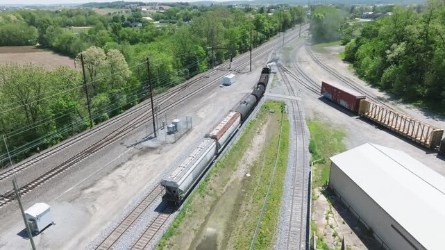 A vintage steam freight train makes its way backing up in yard performing switching operations moving steadily along the railway tracks in a peaceful countryside setting.