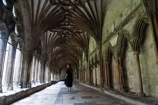 Student in academic dress walking through an ancient gothic cloister, representing education milestone and historic architecture. Canterbury cathedral