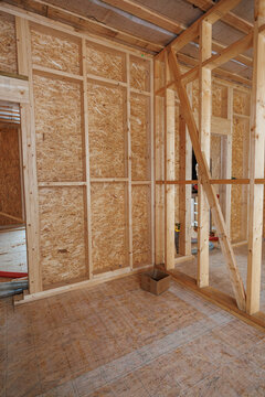 Upright studs, diagonal bracing, and OSB sheathing appear indoors. Cavities prepare for wood fiber loose fill insulation. Exposed subfloor and ducts await install.