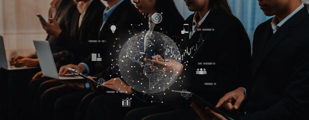 A group of business professionals is engaged with their devices at a conference, surrounded by a digital globe and data icons, symbolizing networking and connectivity. Trope