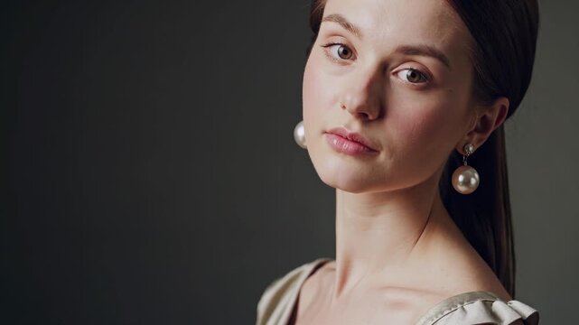 The young woman gazes softly at the camera, showcasing her elegant features. Her stylish earrings and hairstyle complement the woman's poised expression.