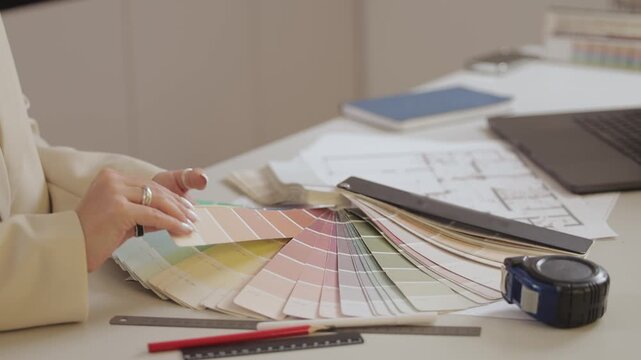 Female interior designer selecting paint colors from swatches in modern office.