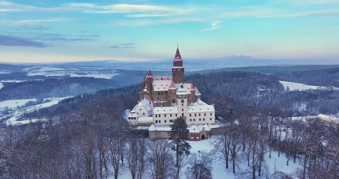 Aerial drone footage of state Bouzov Castle covered in snow at sunrise in  Czech Republic. Cinematic winter landscape with medieval architecture, ideal for: travel films, history, tourism promotion.