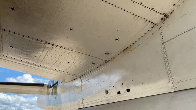 Close view of a vintage military aircraft shows the tail and wing panels with rows of rivets. The metal airframe and camouflage paint highlight classic airplane construction.