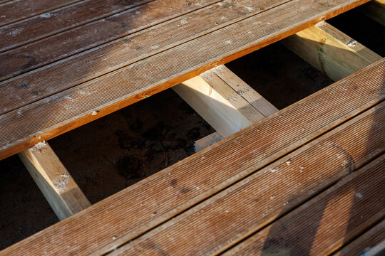Wooden deck section shows removed planks, fresh light joists, sawdust, ridged boards, screw holes, and clean joinery, in warm late afternoon light on a residential deck.