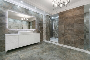 The bathroom is decorated with gray marble tiles. Shower cabin with glass door. The mirror is...