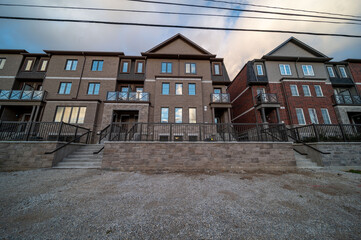 Naklejka premium Row of newly constructed multi story townhouses featuring brick and siding facades, offering contemporary urban housing and residential living spaces under a cloudy sky