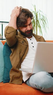Displeased Middle eastern man use laptop notebook typing browsing working, loses becoming surprised sudden lottery results bad news fortune loss game fail computer virus. Young guy on home room couch