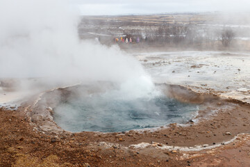 Steam rises from geothermal area in iclenad geysir with tourists in winter landscape