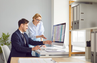 Two young confident business people man and woman working in office sitting at the desk with pc computer with tables and charts on workplace analyzing financial data . Accountant job concept.