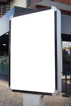 Empty vertical advertising billboard with white space for copy, placed outdoors on a city promenade with palm trees and buildings in the background. Ideal for marketing, branding, poster design