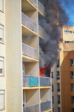 Fire burning on an apartment balcony with heavy black smoke rising along a residential building. Urban emergency situation in a multi-storey housing complex, danger, risk, and safety.