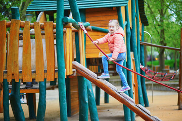 Young girl in a pink jacket climbing up a wooden playground structure using a rope