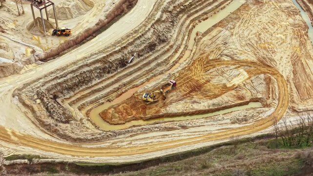 Heavy machinery is at work in a construction area. The vehicles are moving soil and shaping the land near a water source. The site shows patterns from digging and earth removal.