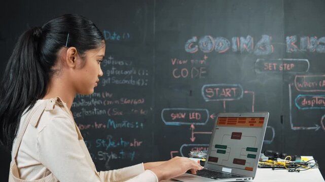 high school girl writing code or engineering prompt while attend in STEM technology class. Teenager coding or programming system while looking at computer screen in front of blackboard. Edification