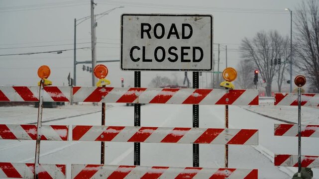 Road closed sign stands behind road closure barriers during snowy winter conditions. traffic restrictions, blocked access due to weather or road work. Close up view