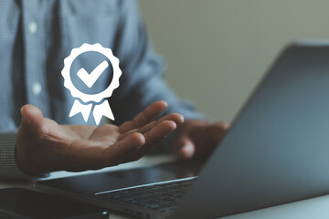 Businessman hand presenting quality certification checkmark icon above laptop, representing approval, trust, compliance, verification, assurance concept for corporate standards professional services.
