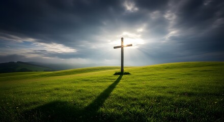 Obraz premium Wooden cross atop a green hill, sun rays shining, dramatic sky, casting a long shadow
