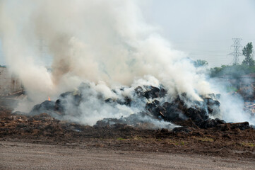 A large heap of hay, wood and debris emits dense smoke on a demolition site creating an industrial, smoky scene. Pollution, waste management and environmental impact in outdoor settings.