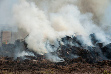 A large heap of hay, wood and debris emits dense smoke on a demolition site creating an industrial, smoky scene. Pollution, waste management and environmental impact in outdoor settings.