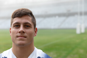 White goalposts standing on grassy pitch with line markings and tiered seating under clouds