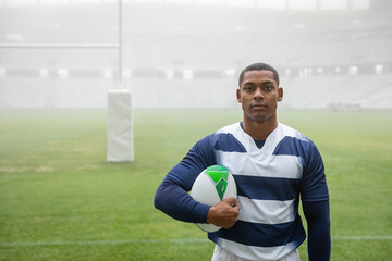 Green and white rugby ball resting on trimmed grass pitch near padded goal post in fog