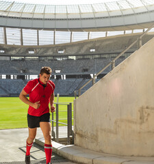 Male athlete is running up concrete ramp inside covered stadium, sunlight illuminating grass pitch