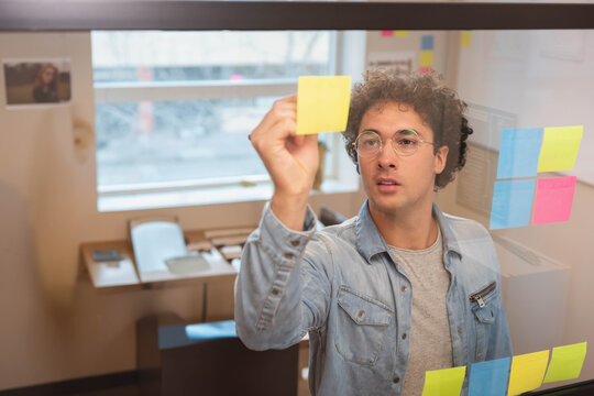 Colorful sticky notes are being placed on glass partition in small office with desk
