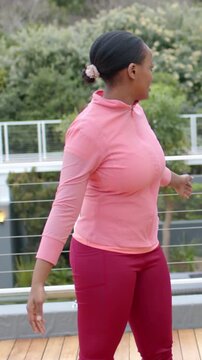 Vertical video: Warming woman in pink top leggings turning and raising arm on deck railing hair tie