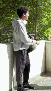 Vertical video: Adjusting headset, teen in hoodie greeting friend arriving with football on terrace
