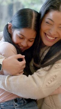 Vertical video: Leaning mom in knit sweater whispering comfort, hugging girl in pink top on couch