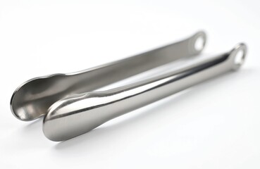 Pair of stainless steel tongs rests on a clean white surface. This metallic kitchen tool is ideal for serving food or ice cubes with ease and hygiene.