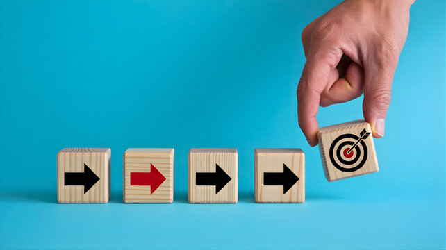 Hand placing a wooden block with a target on it at the end of a line of blocks with arrows, representing achieving a goal