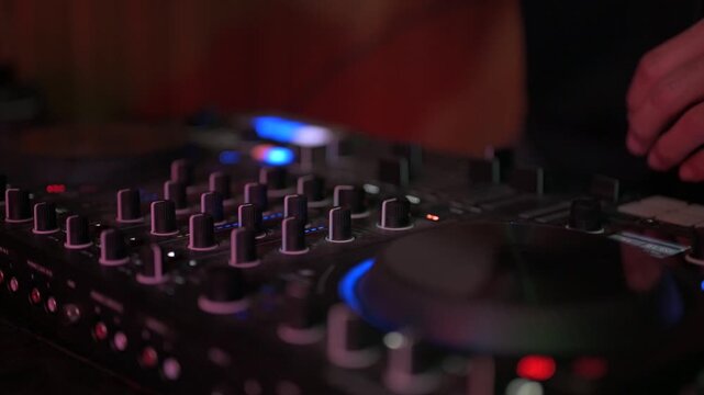 Close up of a disc jockey's hands skillfully manipulating the knobs and faders on a professional sound mixing console, creating electronic music during a performance in a dimly lit club