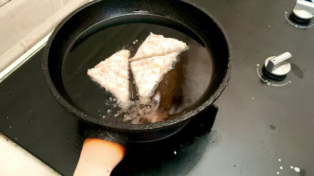 hand placing triangle cut tempeh into hot oil in a frying pan for deep frying